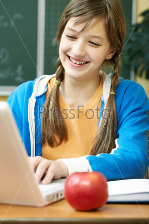Portrait of clever girl sitting at lesson and looking at laptop monitor