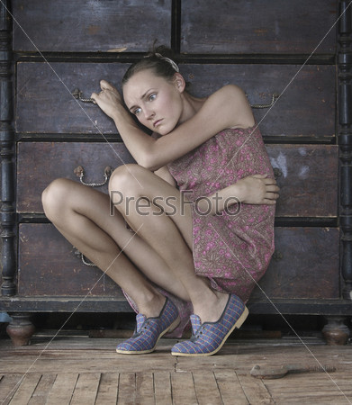 Fashion type photo of an attractive young woman sitting near an old chest of drawers