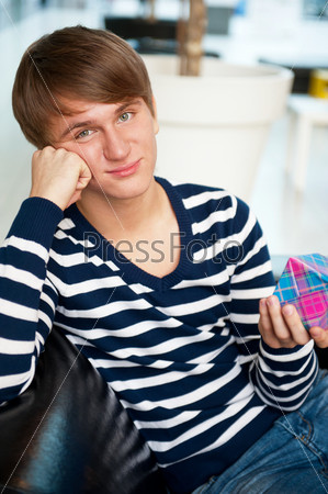 Portrait of young man inside shopping mall sitting relaxed on couch, holding box and preparing to make his couple a gift.