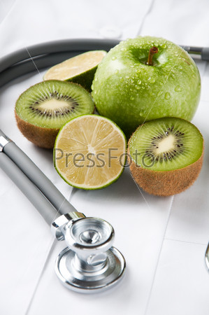 Fresh apple, kiwi, lime and stethoscope on doctor\'s smock