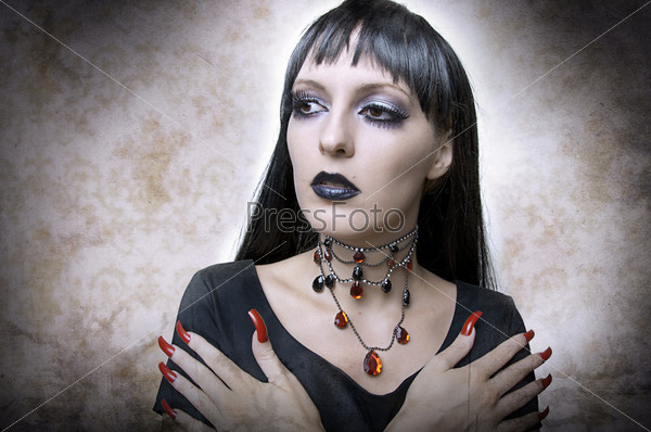 Halloween concept. Fashion portrait of gothic style woman night vampire or evil witch in black dress and vintage necklace. Brunette with long health hair.