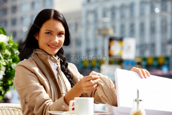 Image of happy female in open air cafe taking out gift out of box outdoor