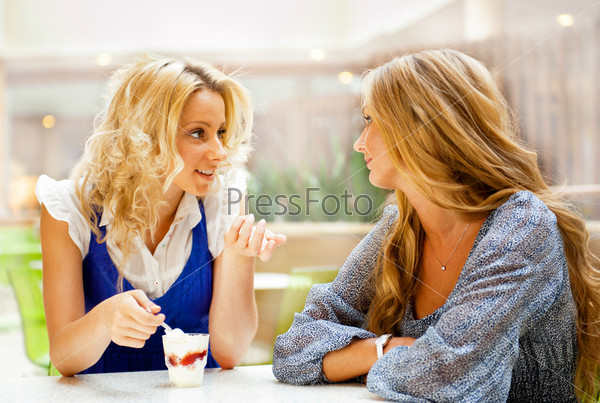 Two beautiful women drinking coffee and chatting at mall cafe.