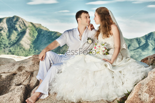 Bride and groom sitting on the rock. Mountain on background