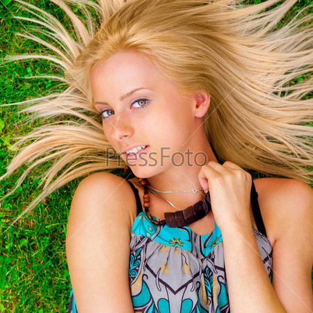 Young woman laying on green grass with hair like a sun around her head. Photo from above