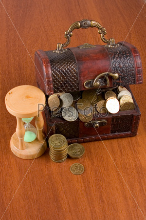 Open chest with coins and  hourglass on a wooden surface close-up