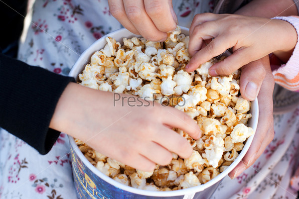Children eat popcorn out of a paper bucket, close-up