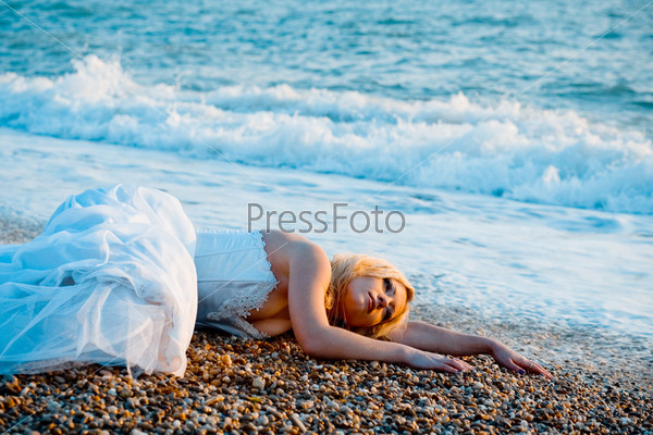 Trash the wedding dress series. Tired bride lying on ocean coast near sea waves.