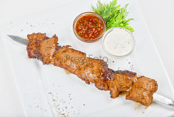 Grilled pork kebab with sauce nad greens on white plate