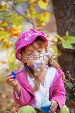 Funny child blowing soap bubbles in autumn park