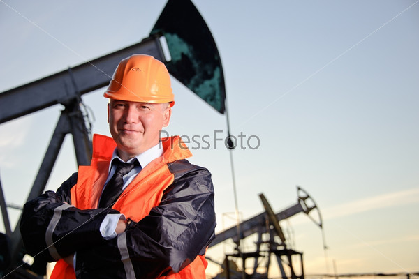 Нефтяник в оранжевой форме и каске на фоне нефтяных скважин