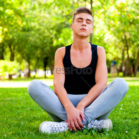 Beautiful young man in meditation pose outdoors.