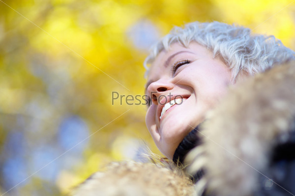 Smiling blond looks into the distance against the backdrop of yellow leaves
