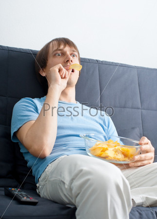 Young surprised man watching tv and eating chips
