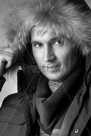 Fashion closeup  portrait of young handsome man in black fur hood winter jacket. Black and white