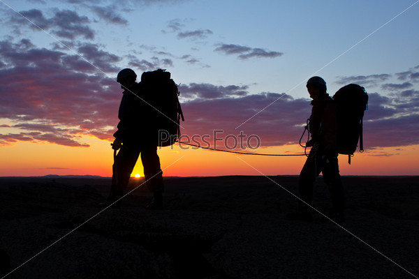 Two climbers walk on sunset\'s background