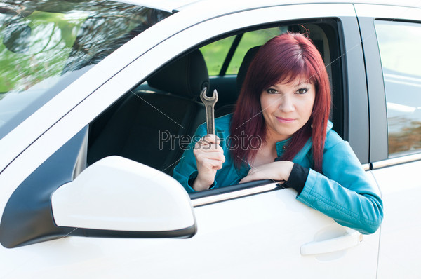 Portrait of a bewildered young woman sitting in a car outdoors with a wrench in her hand