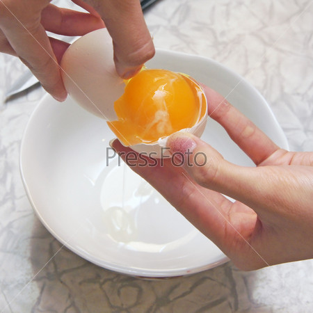 The girl breaks egg in a cup