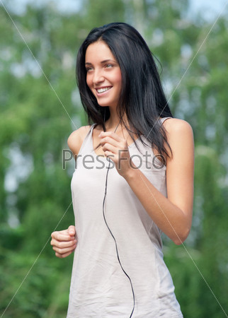Young beautiful woman running in park and listening to music