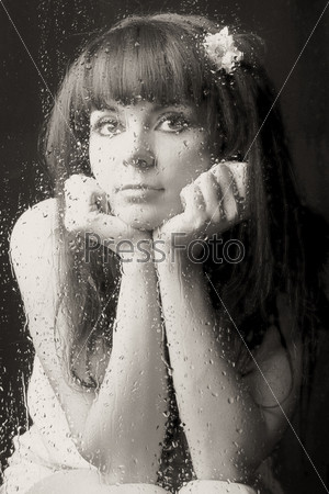 The beautiful woman sits at window. On which glass drops of a rain flow and dreams.