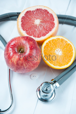 Fresh fruits and stethoscope lying on doctor\'s smock