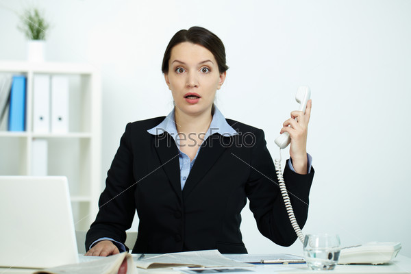 Portrait of amazed office worker with phone receiver looking at camera