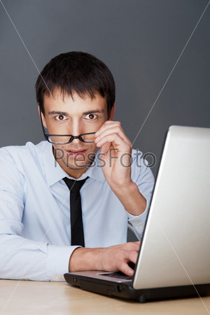 Portrait of a adult excited business man sitting by his laptop in the office and looking at camera expecting something