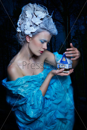 fantasy portrait of beautiful young woman imaging ice fairy on frozen blue with toy house in the night forest