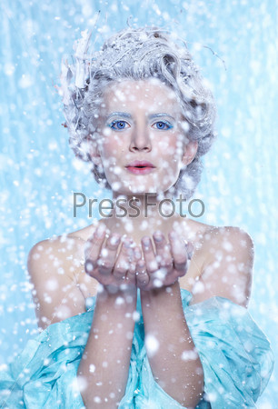 fantasy portrait of beautiful young woman imaging ice fairy on frozen blue blowing snow from hands