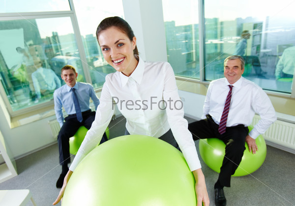 Portrait of pretty female with big ball looking at camera and smiling with her colleagues behind