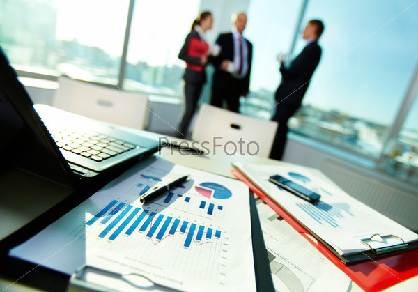 Image Of Business Documents On Workplace With Three Partners Interacting On Back
