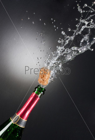 Бутылка шампанского с вылетающей пробкой и брызгами на черном фоне