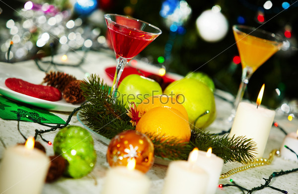 Image of holiday table with cocktails, fruits, burning candles and decorations on it