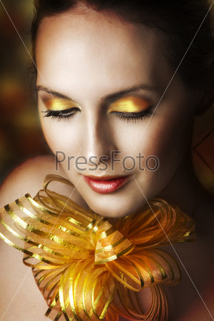 Glamour portrait of young fashion woman face with bright evening golden make up for party and gold ribbon on neck. Concept - make-up as christmas gift