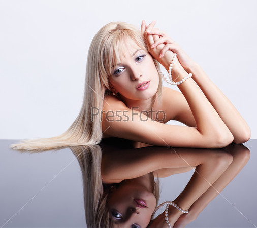 portrait of young beautiful long-haired blonde woman sitting with pearl beads at reflecting table