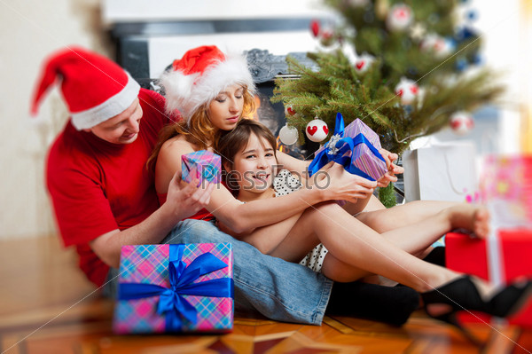 Young happy family near a Christmas tree at home holding gift an