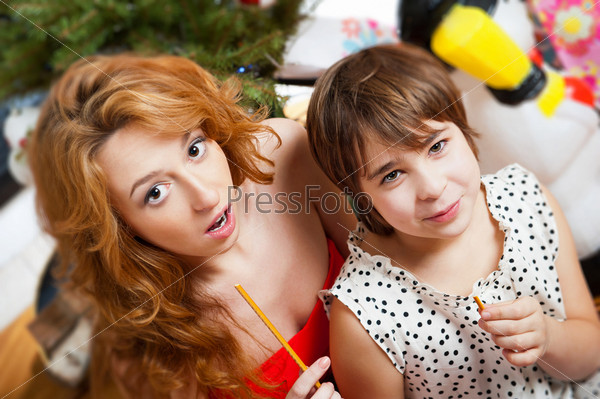 Mother and her daughter sitting together near christmas tree. Top view