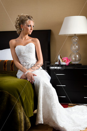 Beautiful woman in a wedding dress. She is in the bedroom with..