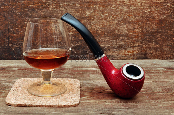 pipe and glass of cognac on wood background
