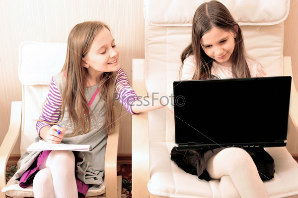Two young girl doing their work on laptop sitting on an armchair