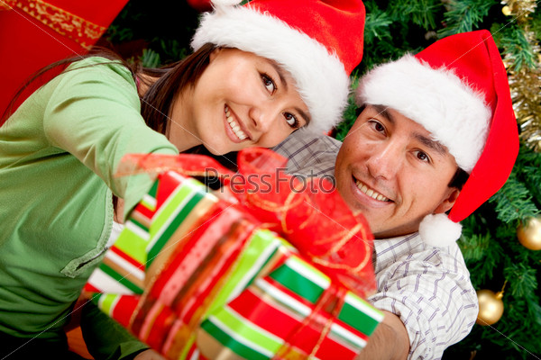 Christmas couple next to the tree with hats and a present