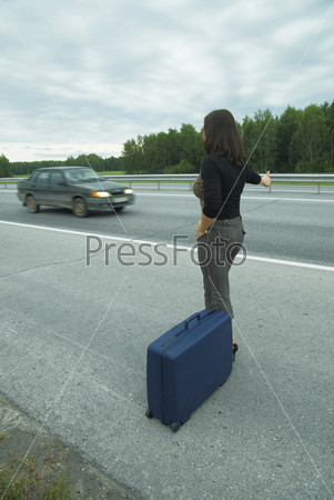 Женщина с чемоданом ловит машину на дороге
