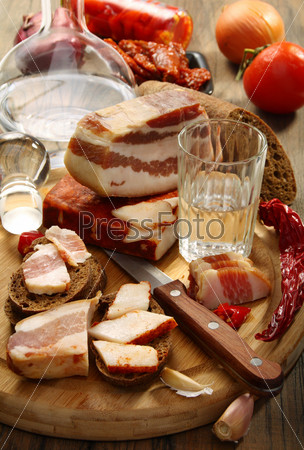 Glass of vodka, bacon on rye bread on a wooden board.