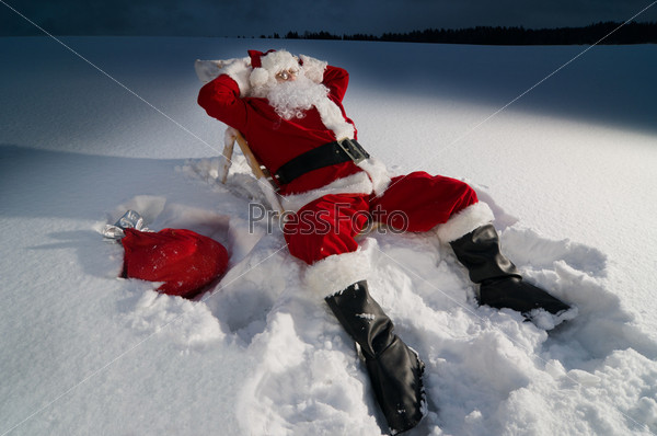 Santa claus relaxing on a sunbed in snow at night, stock photo