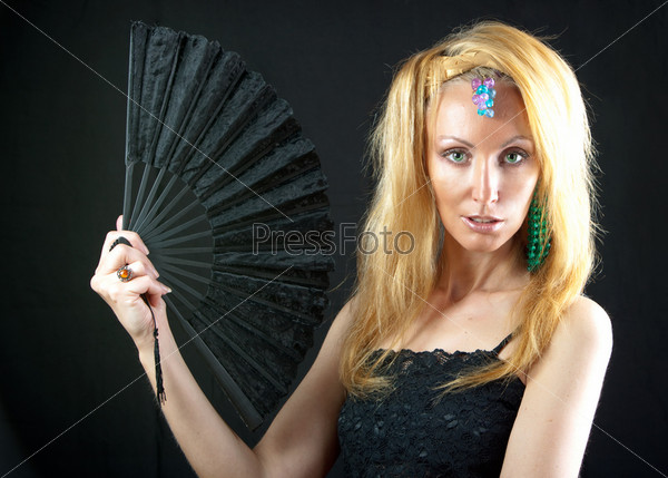 The beautiful young woman with long  blonde hair and  fan and jewellry on  dark background
