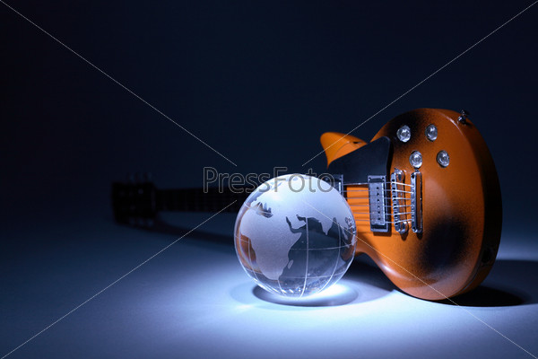 Music concept. Glass globe near electric guitar under beam of light on dark background