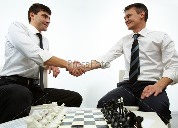 Two men handshaking with chess figures on chess board near by