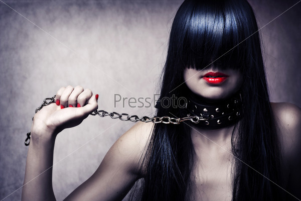 Fashion portrait of young beautiful female model. Glamour woman with long black hair and sexy hairstyle. Lady with leather collar with studs on a metal chain in hand