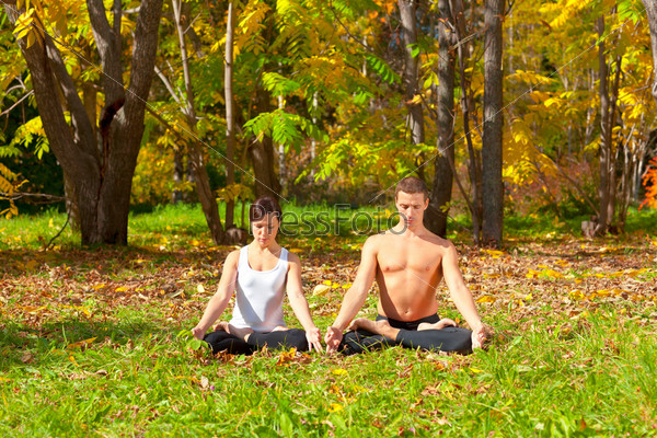 An attractive  man and woman practice Yoga padmasana pose in forest
