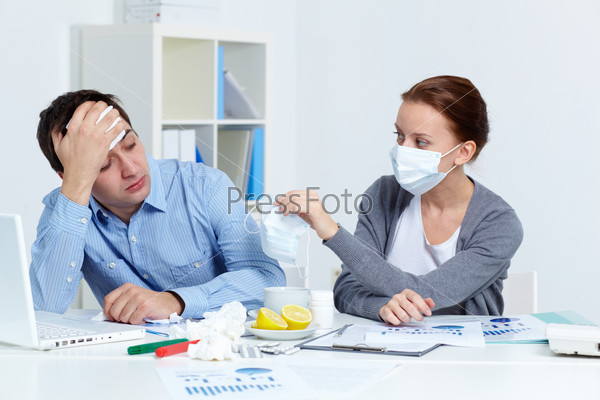 Image of sick businessman looking at his partner in mask offering him to put on one in office